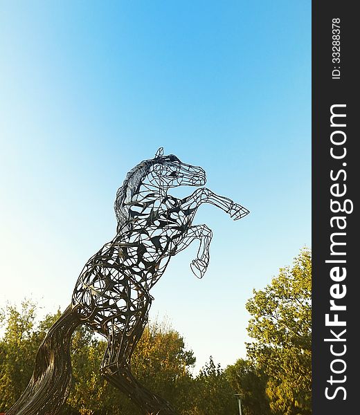 A horse statue made of metal in the park against a blue sky. A horse statue made of metal in the park against a blue sky