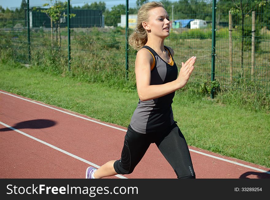 Runner, young female with blond hairs running on the track, wearing sport's outfit. Runner, young female with blond hairs running on the track, wearing sport's outfit.
