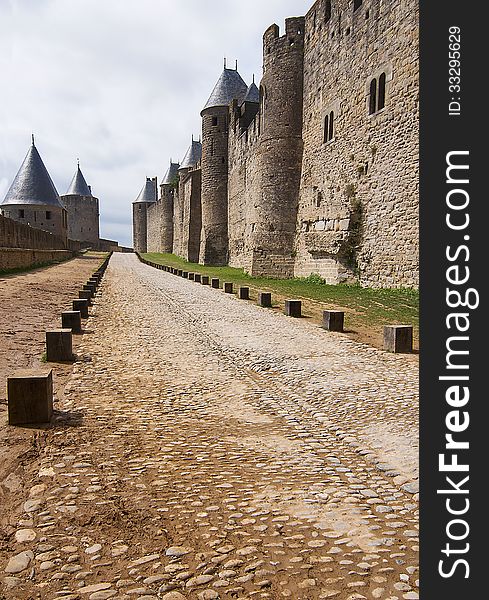 Road between inner defense wall with conic towers and outer frontier of Carcasson castle in green grass with shades. Road between inner defense wall with conic towers and outer frontier of Carcasson castle in green grass with shades