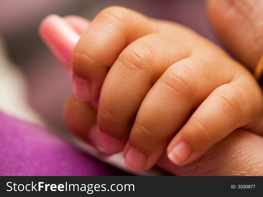 Tiny newborn baby fingers wrapped around adult female fingers up close. Tiny newborn baby fingers wrapped around adult female fingers up close