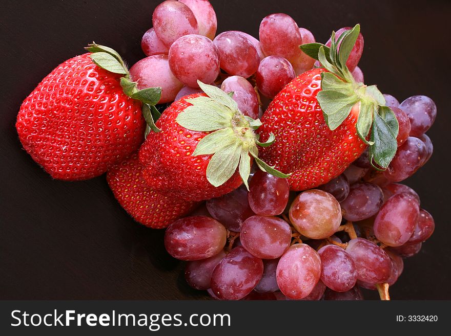 Large strawberries and red grapes on a dark surface