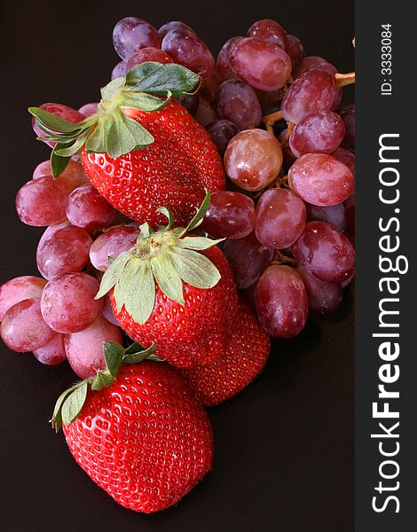 Healthy strawberries and red grapes on a dark surface. Healthy strawberries and red grapes on a dark surface