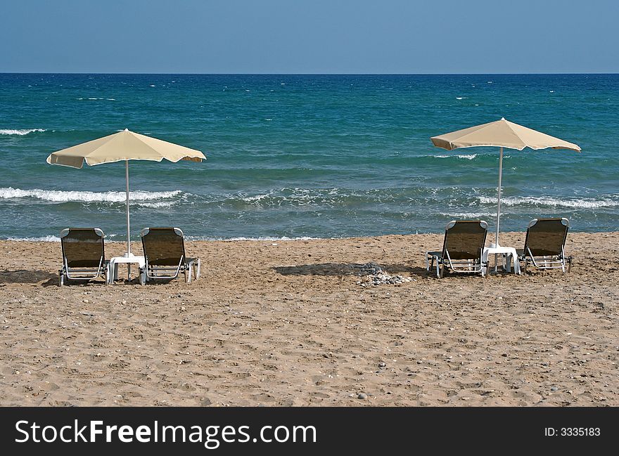 Two umbrellas with chairs on the beach facing blue sea. Two umbrellas with chairs on the beach facing blue sea