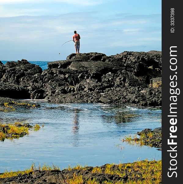 Man using rod and reel to fish from atop lava outcropping. Man using rod and reel to fish from atop lava outcropping