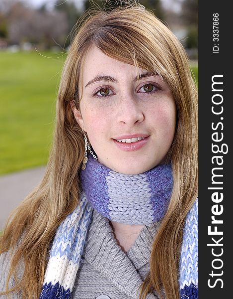 Young beautiful teen outdoors at the park with a different pose, scarf, and sweater. Has a fall or winter season look.