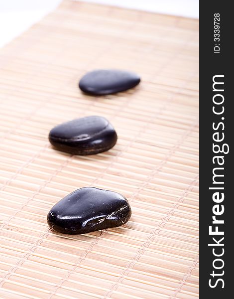 Three smooth, black Zen-Stones (Pebbles) in a row on a bamboomat. Focus on front stone. Three smooth, black Zen-Stones (Pebbles) in a row on a bamboomat. Focus on front stone.