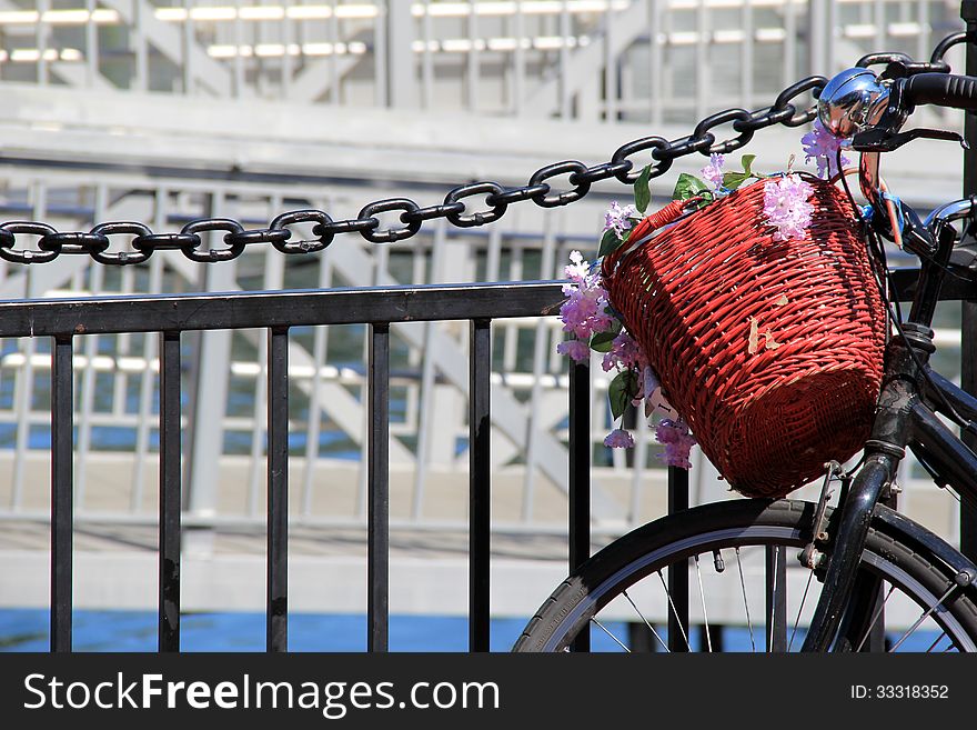 Pretty little basket holding flowers on the handlebars of an old bicycle,set against fencing near the water. Pretty little basket holding flowers on the handlebars of an old bicycle,set against fencing near the water.