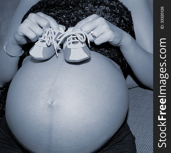 Pregnant woman shows her belly with baby's shoes
