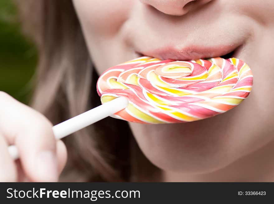 Girl holds a color lollipop in his mouth