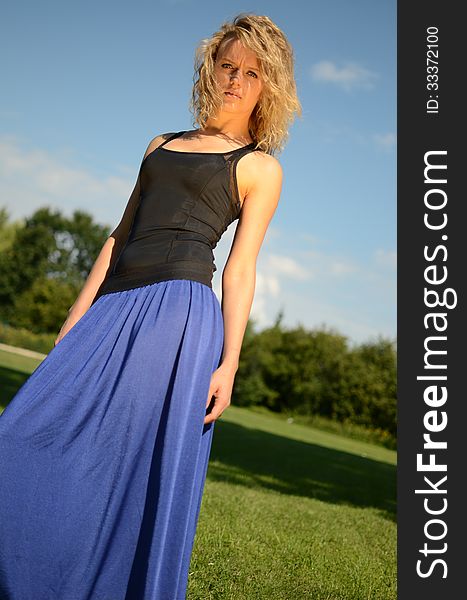 Female model with blond, curly hairs. Girl wearing blue dress and black top. Outdoor photo session in the park with blue sky as background. Female model with blond, curly hairs. Girl wearing blue dress and black top. Outdoor photo session in the park with blue sky as background.