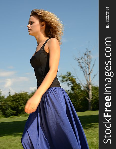 Female model with blond, curly hairs. Girl wearing blue dress and black top. Outdoor photo session in the park with blue sky as background. Female model with blond, curly hairs. Girl wearing blue dress and black top. Outdoor photo session in the park with blue sky as background.