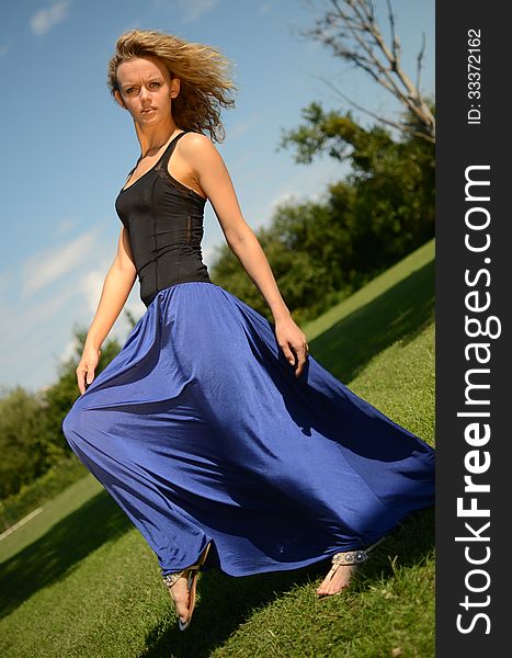 Female model with blond, curly hairs. Girl wearing blue dress and black top. Outdoor photo session in the park with blue sky as background. Female model with blond, curly hairs. Girl wearing blue dress and black top. Outdoor photo session in the park with blue sky as background.