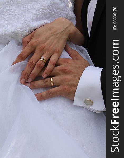 Gold wedding rings placed on the fingers of the bride and groom. Groom's hand is placed on the bride's white wedding dress