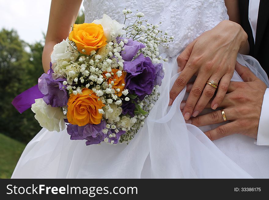 A beautiful image of the hands of the bride and groom that have on their fingers the gold wedding rings and the bride is holding near her body the wedding bridal bouquet. A beautiful image of the hands of the bride and groom that have on their fingers the gold wedding rings and the bride is holding near her body the wedding bridal bouquet.