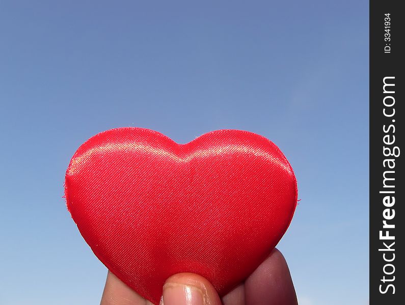 A red fabric little heart with the sky background for saint Valentine's Day, representing love. A red fabric little heart with the sky background for saint Valentine's Day, representing love