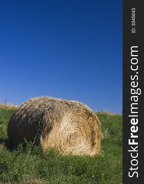 A roll of hay stands on green grass against a deep blue sky.