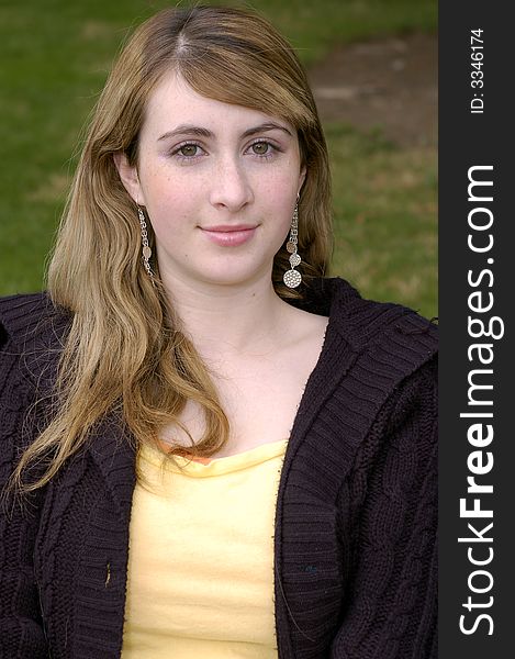 Young beautiful teen outdoors at the park with a different view, pose, and black sweater. Has a fall or winter season look.