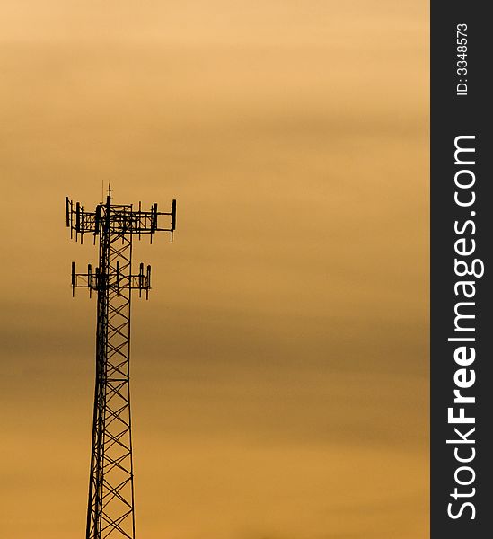 A view of the top of a tall telecommunications tower with several cellphone transmitting and receiving antennas, against an orange, sunset sky. A view of the top of a tall telecommunications tower with several cellphone transmitting and receiving antennas, against an orange, sunset sky.