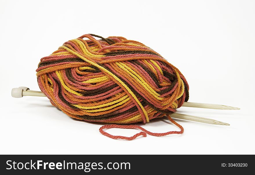 Ball of multicolored yarn in brown, yellow, and orange tones with a pair of wooden knitting needles against a white background. Ball of multicolored yarn in brown, yellow, and orange tones with a pair of wooden knitting needles against a white background