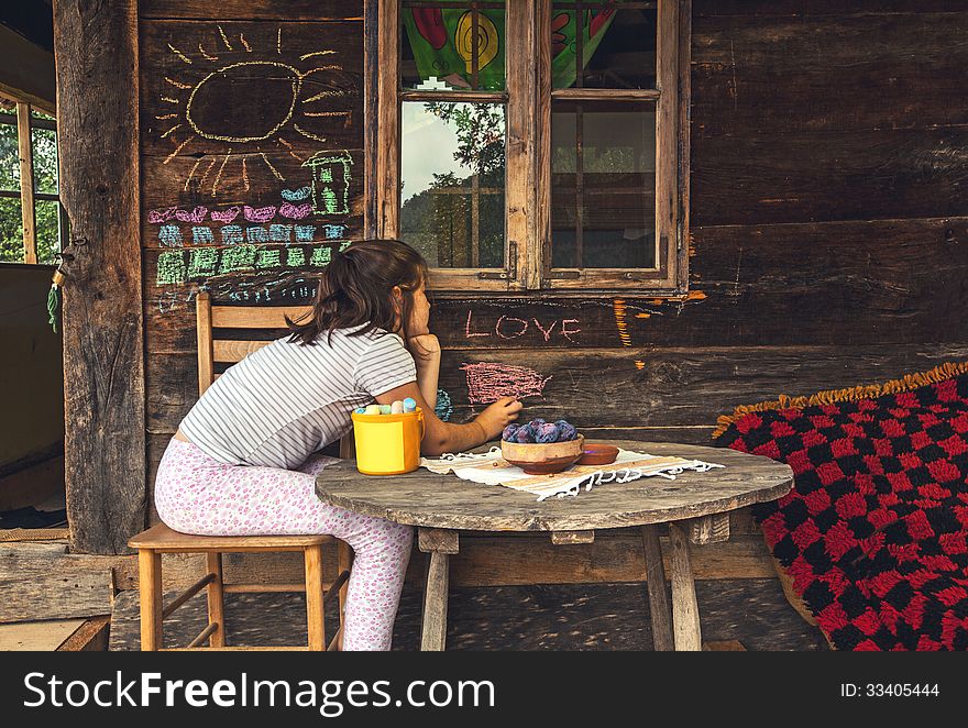 Child in front of a wooden house, playing and painting with chalk on wall. Child in front of a wooden house, playing and painting with chalk on wall.