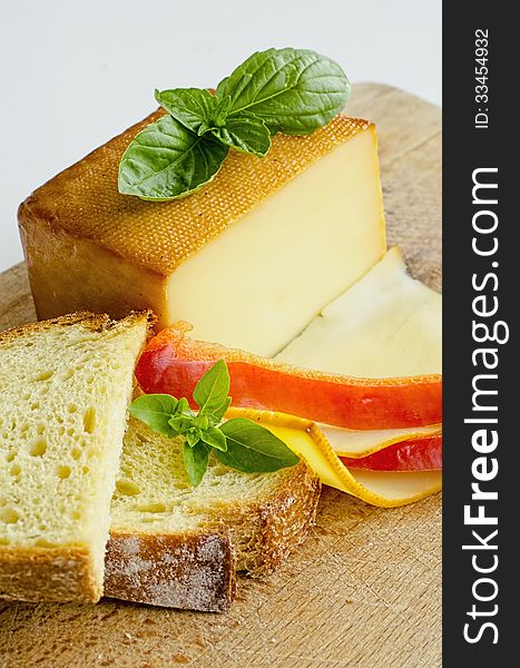 Smoked full fat cheese, a couple of slices and piece, healthy homemade bread, fresh red pepper and fresh, green basil leaves on grunge wooden chopping board, vertical orientation. Smoked full fat cheese, a couple of slices and piece, healthy homemade bread, fresh red pepper and fresh, green basil leaves on grunge wooden chopping board, vertical orientation