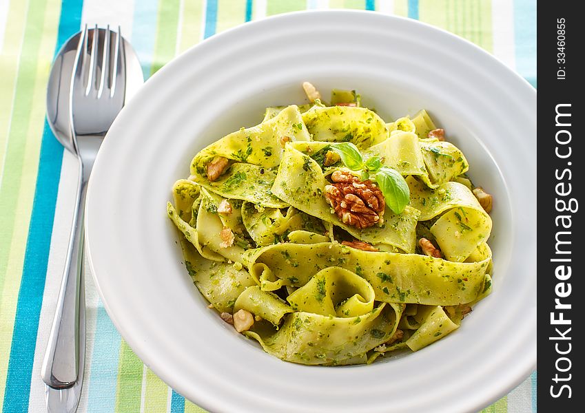 Tagliatelle pasta with pesto and walnuts on white plate. Tagliatelle pasta with pesto and walnuts on white plate