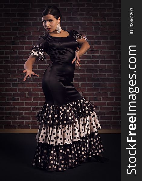 Beautiful modern spanish flamenco dancer wearing brown color silk dress with polka dots doing a line pose. Isolated over red brick wall background.