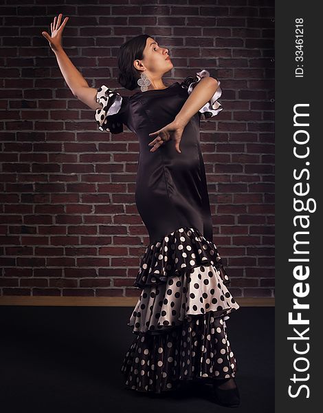 Beautiful modern spanish flamenco dancer wearing brown color silk dress with polka dots doing a line pose. Isolated over red brick wall background. Beautiful modern spanish flamenco dancer wearing brown color silk dress with polka dots doing a line pose. Isolated over red brick wall background.