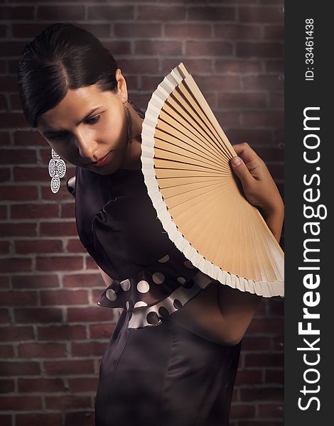 Young beautiful woman,a flamenco dancer is standing in pose with hand fan, looking over her shoulder. Red brick wall background. Young beautiful woman,a flamenco dancer is standing in pose with hand fan, looking over her shoulder. Red brick wall background.