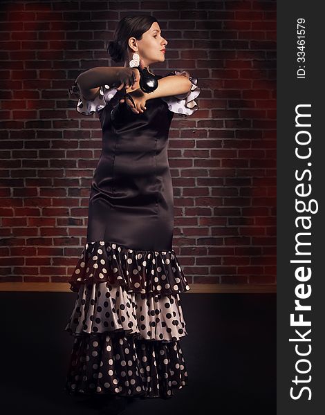 Young woman in beautiful dress performs Spanish dance with castanets. Red brick wall background. Young woman in beautiful dress performs Spanish dance with castanets. Red brick wall background.