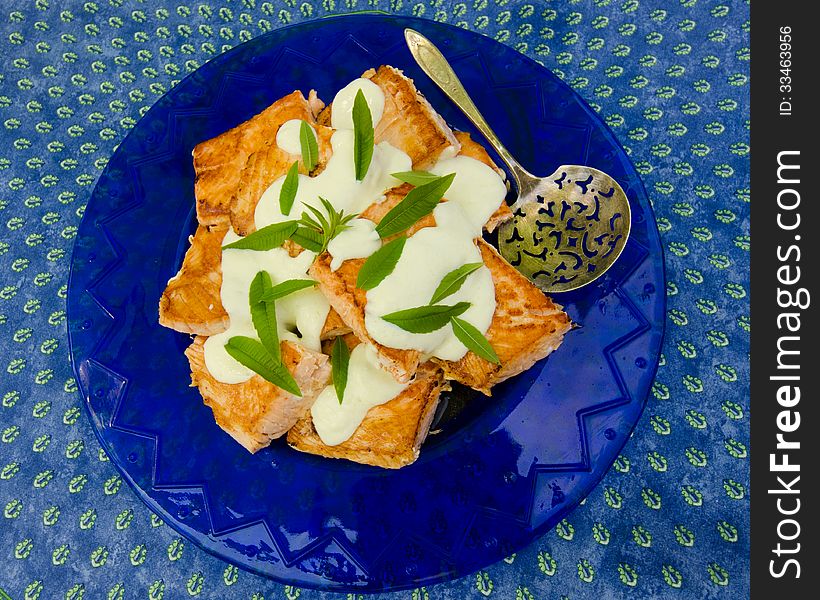 Close-up of baked salmon with lemon sauce and mint served on a blue plate.