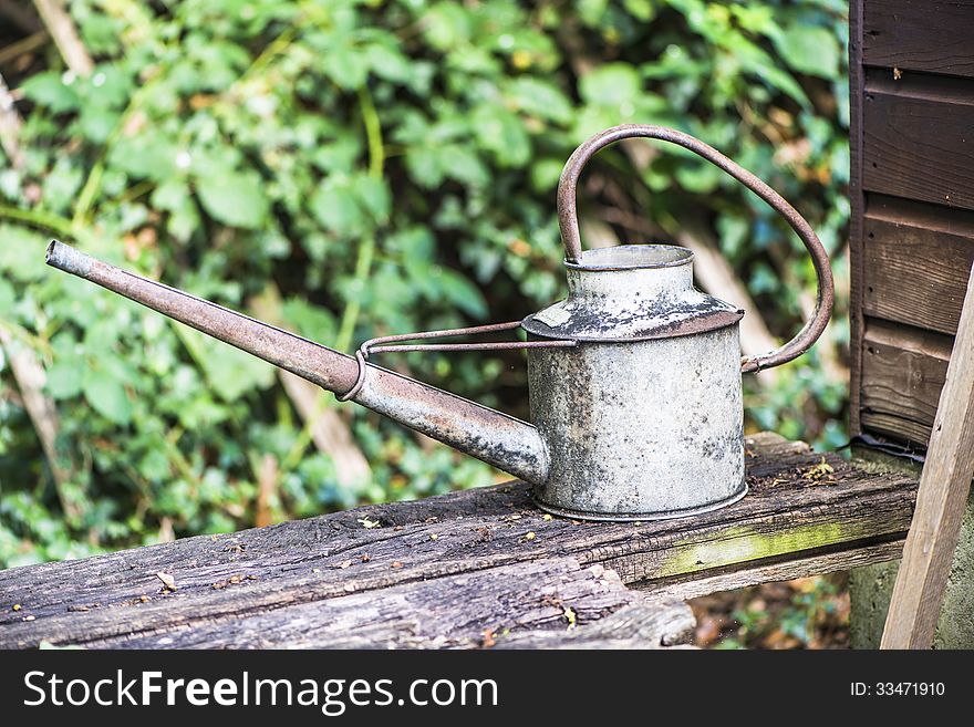 Old buttered watering can on broken wooden bench in the garden