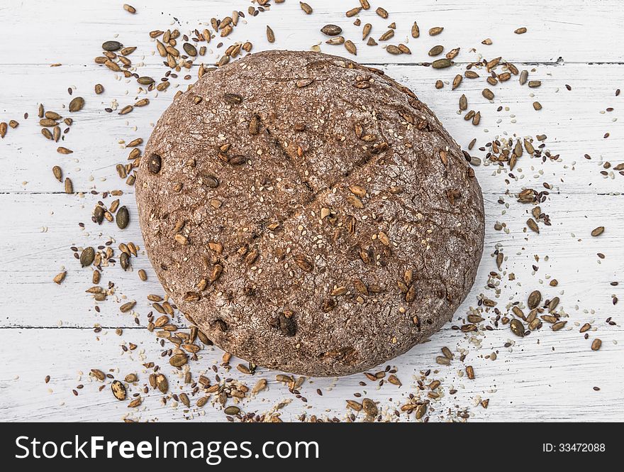 Wholemeal bread with seeds scattered around it on white wooden board. Wholemeal bread with seeds scattered around it on white wooden board