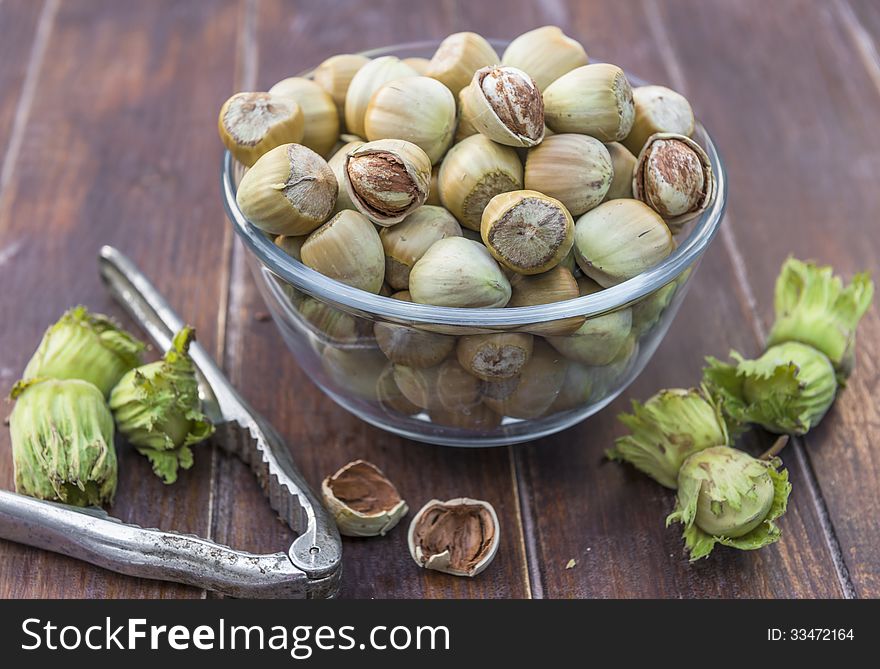 A bowl of fresh hazelnuts and a nut cracker on wooden table