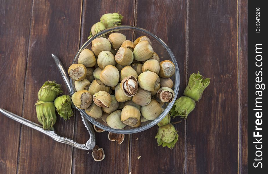 A bowl of fresh hazelnuts and a nut cracker on wooden table