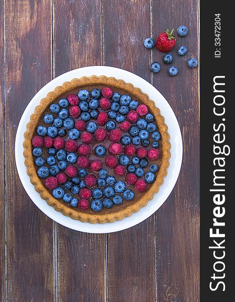 A cake garnished with summer fruit - raspberries and blueberries on wooden table