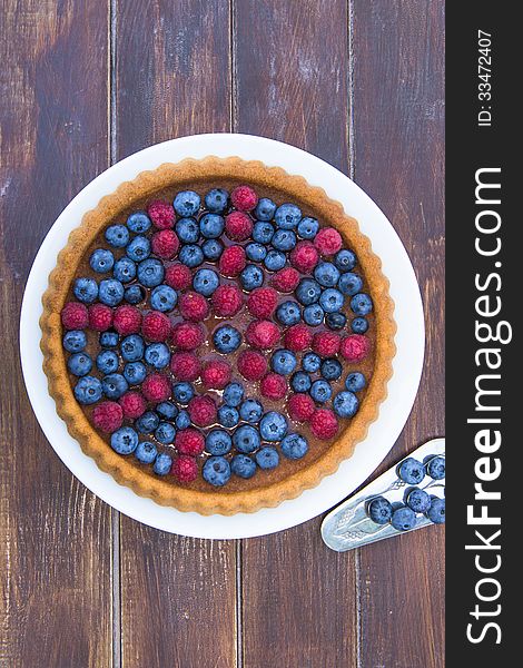 A cake garnished with summer fruit - raspberries and blueberries on wooden table