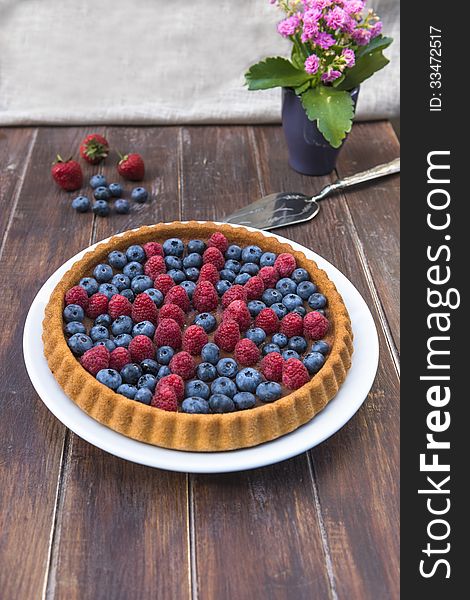 A cake garnished with summer fruit - raspberries and blueberries on wooden table