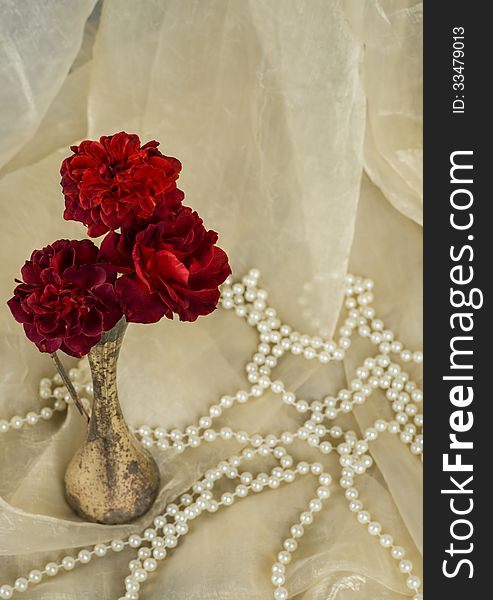 Red roses in an antique silver vase with pearls on cream colored fabric