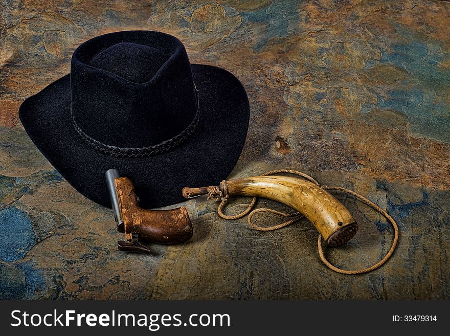 Antique pistol and powder horn with cowboy hat on slate flooring