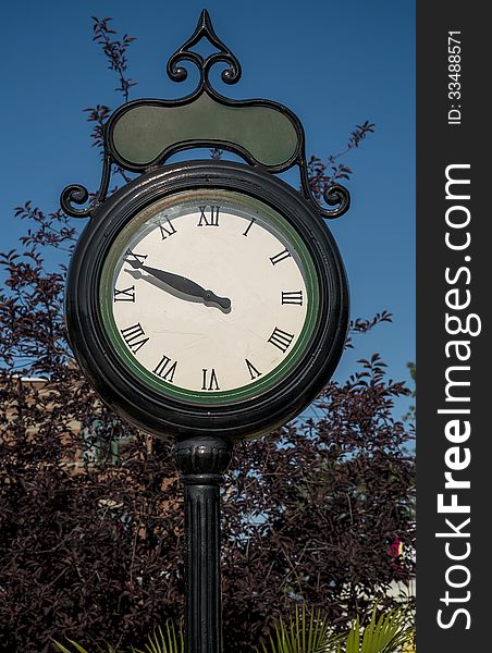 Street clock against blue sky with trees and plants
