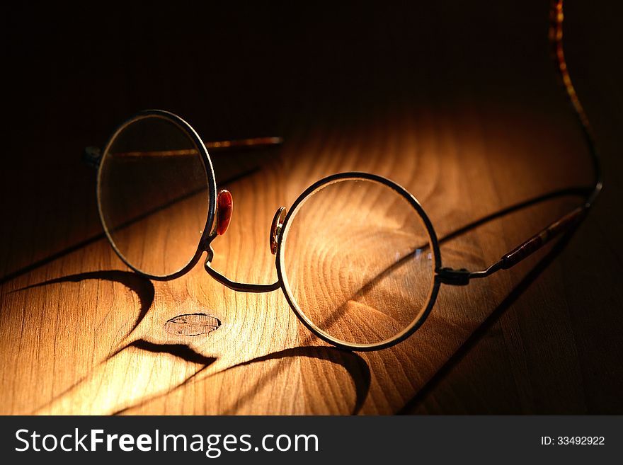 Closeup of old spectacles with long shadow on wooden surface