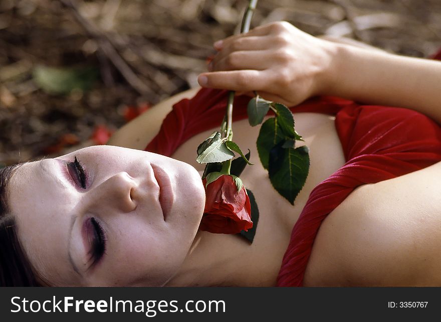 Young woman with red dress laying in the forest, holding a rose. Young woman with red dress laying in the forest, holding a rose.