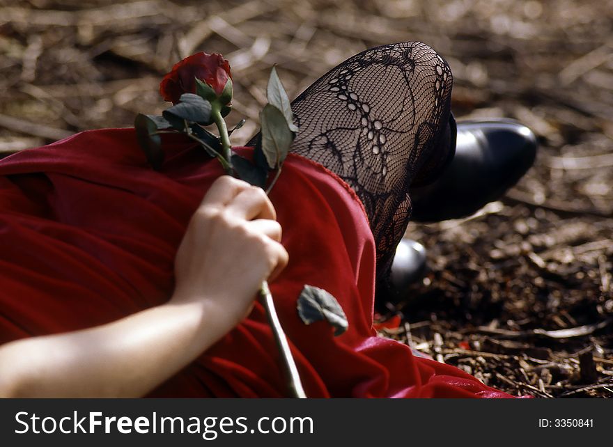 Young woman with red dress laying in the forest, holding a rose. Young woman with red dress laying in the forest, holding a rose.