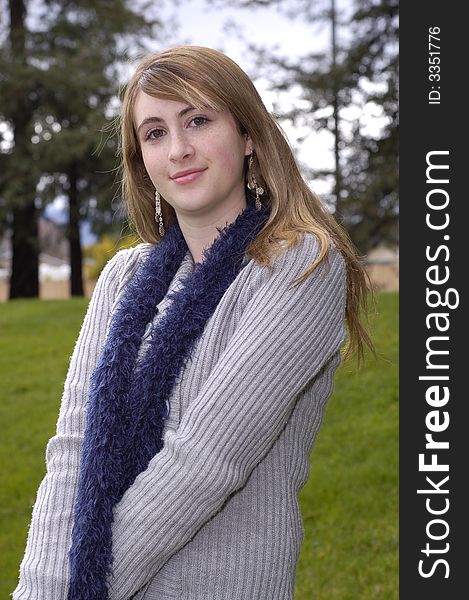 Young beautiful teen outdoors at the park wearing a blue scarf and gray sweater. Has a fall or winter season look.