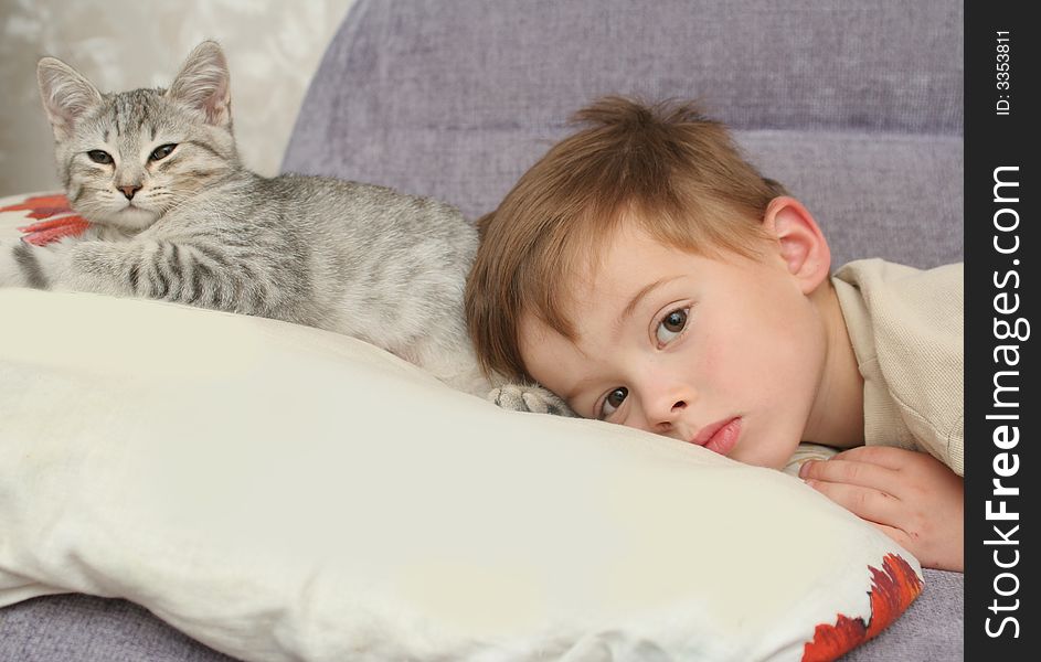 The boy lays on a pillow together with a kitten