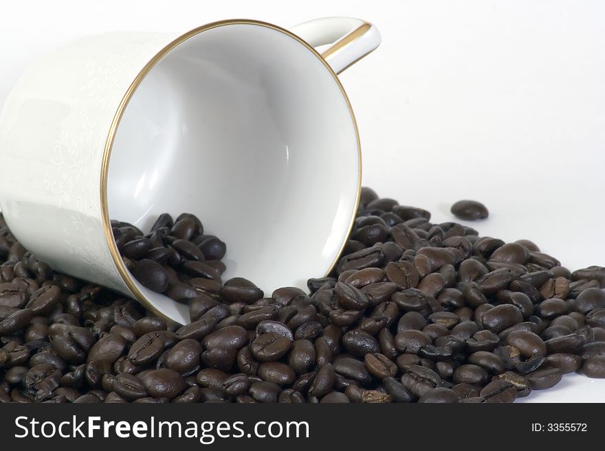 Coffee cup on it's side laying in a pile of coffee beans. Coffee cup on it's side laying in a pile of coffee beans