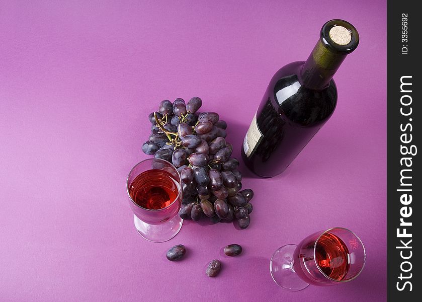 2 glasses of wine, bottle of wine and grape on the violet background