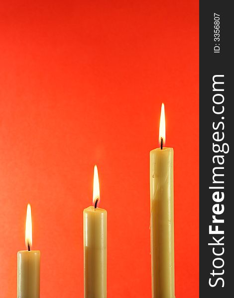 Three burning candles over light red background