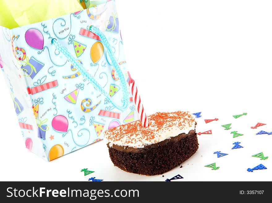 Party hat confetti surrounding a small birthday cake with a single candle and a wrapped gift. Party hat confetti surrounding a small birthday cake with a single candle and a wrapped gift.